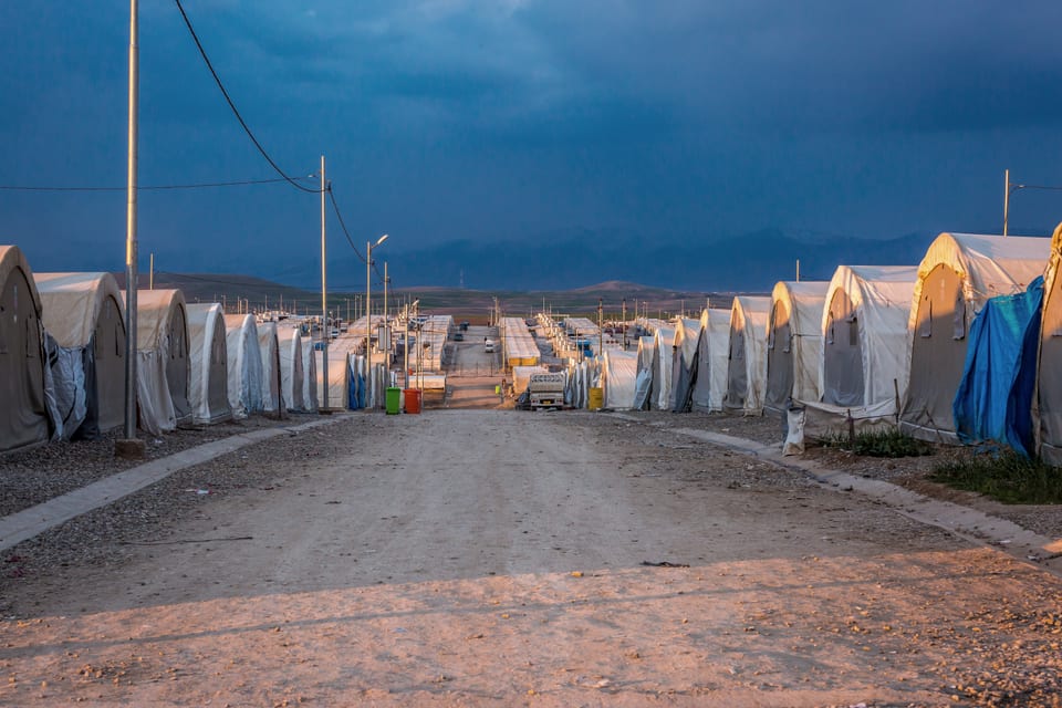 Rows of white tents along a camp road at dusk.