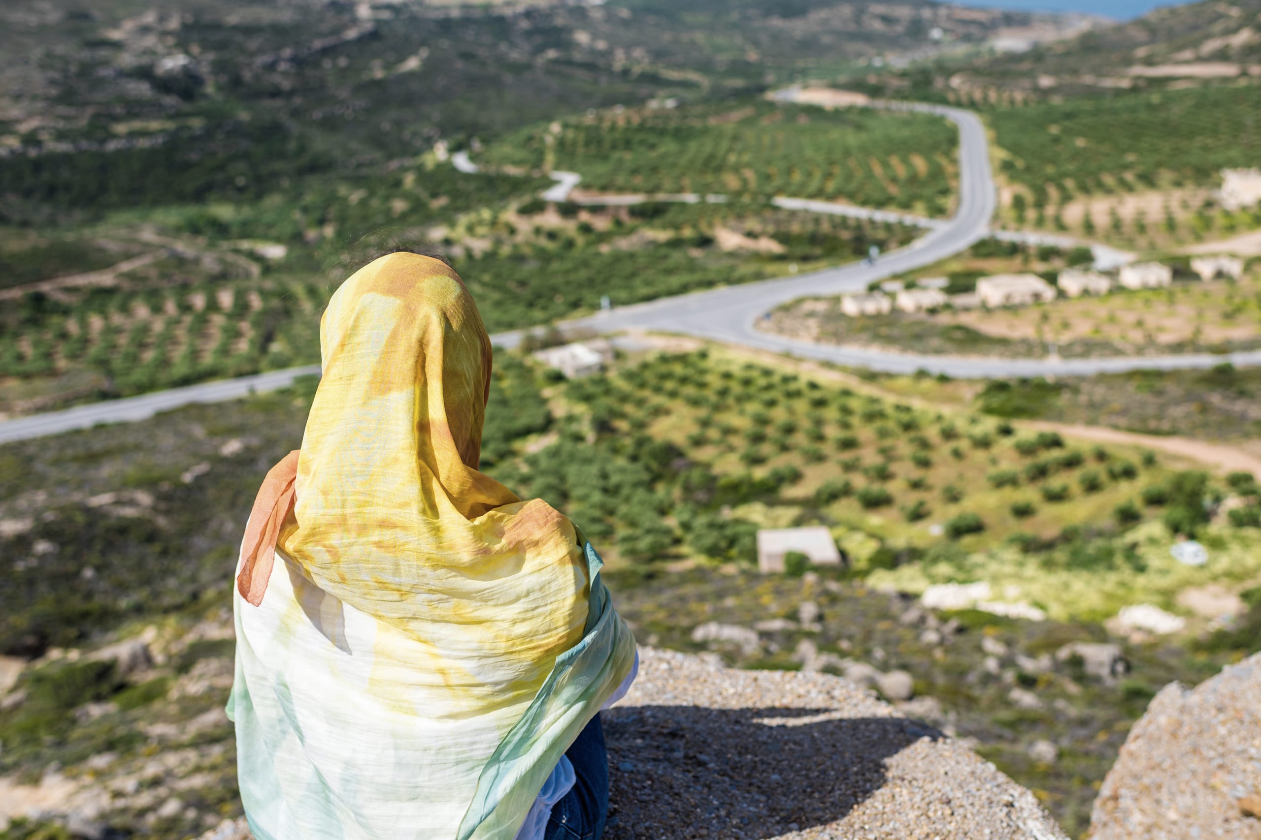 A woman in a headscarf standing above a wide river valley in Iraq, looking out over the fields below.